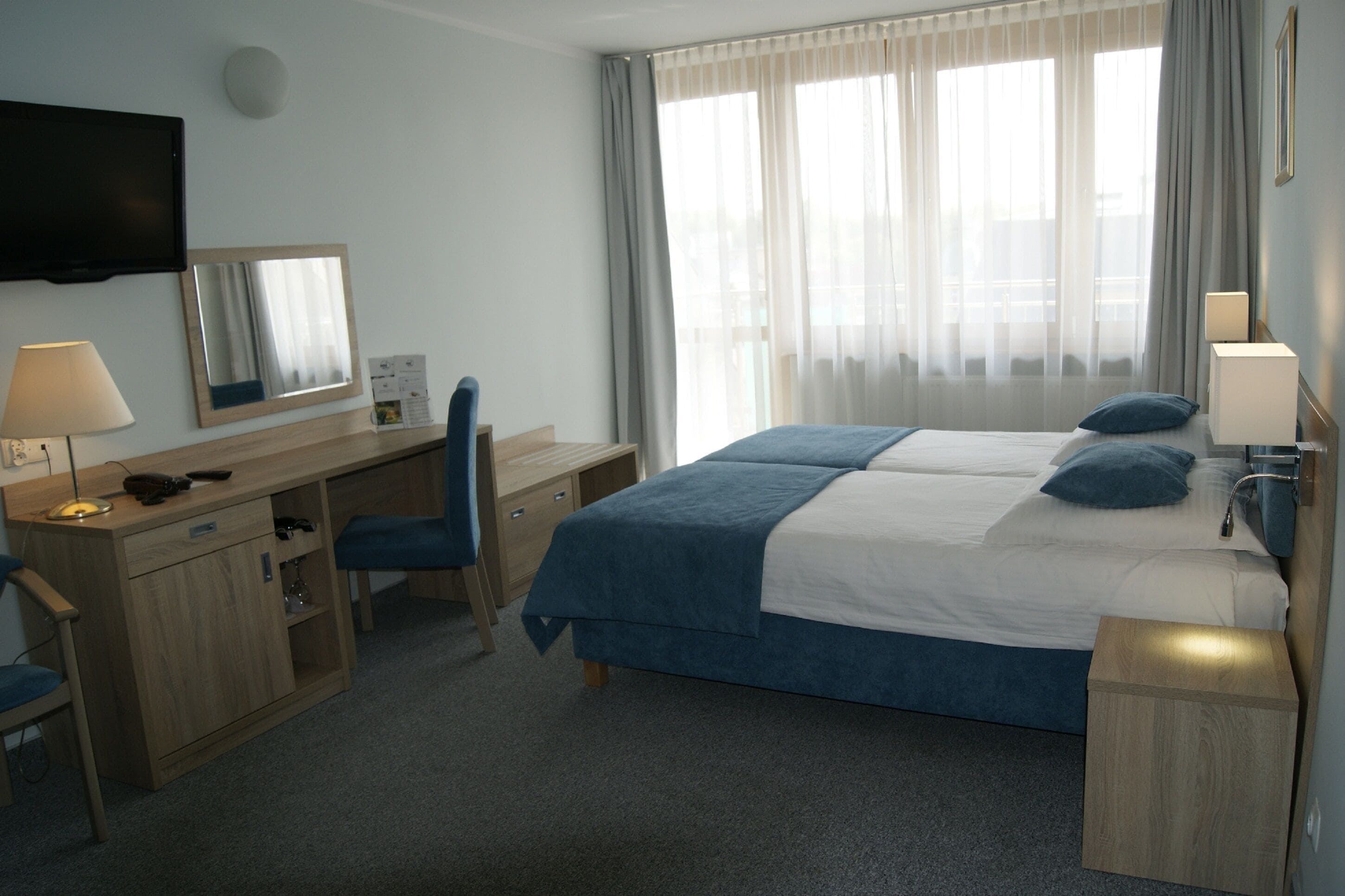 A hotel room with a bed, desk, chair, and a TV mounted on the wall.