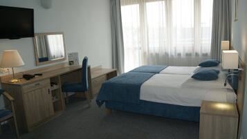 A hotel room with a bed, desk, chair, and a TV mounted on the wall.