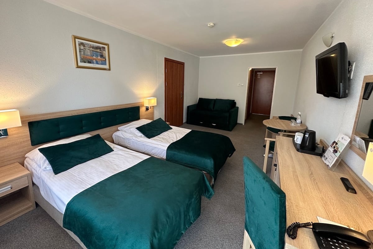 Ein Hotelzimmer mit zwei Betten, einem Schreibtisch, einem Stuhl, einem Fernseher und einer Tür zu einem weiteren Raum.