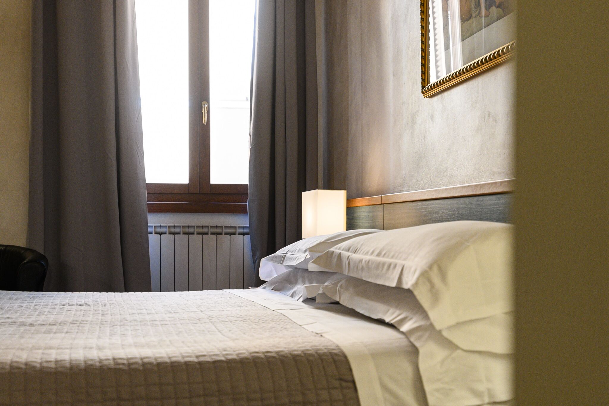 A hotel room with a bed, a nightstand, a lamp, and a window with curtains.