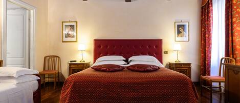 A bedroom with a red upholstered bed, two bedside tables with lamps, a wooden chair, and a door.