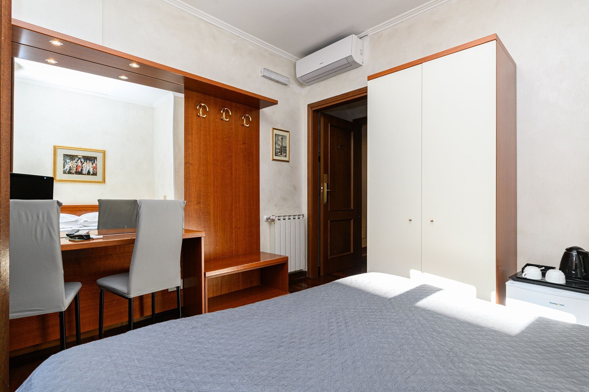 A hotel room with a bed, a desk with two chairs, a wardrobe, a radiator, and a coffee maker.