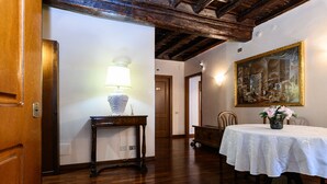 Una habitación con piso de madera, una mesa con mantel blanco, una lámpara y un cuadro en la pared.