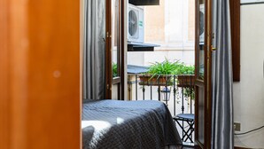 Una habitación con cama, una mesita y un balcón con plantas.