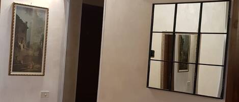 A room with a wooden ceiling, a table with chairs, a framed painting, and a mirror on the wall.