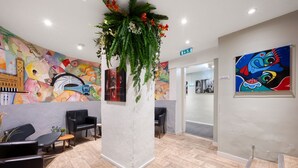 A modern lobby with a colorful mural, a reception desk, and a seating area. - City Hostel (Stockholm)