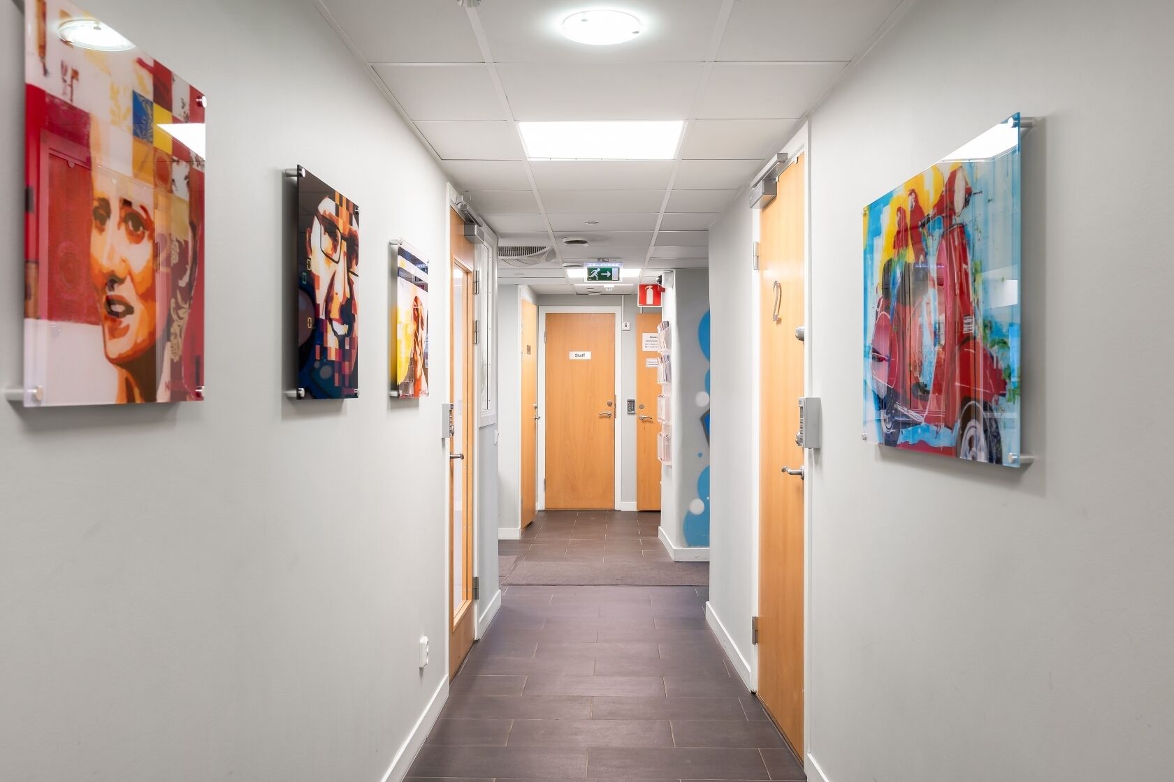 A hallway with artwork on the walls, a wooden door labeled 'Staff,' and a tiled floor.