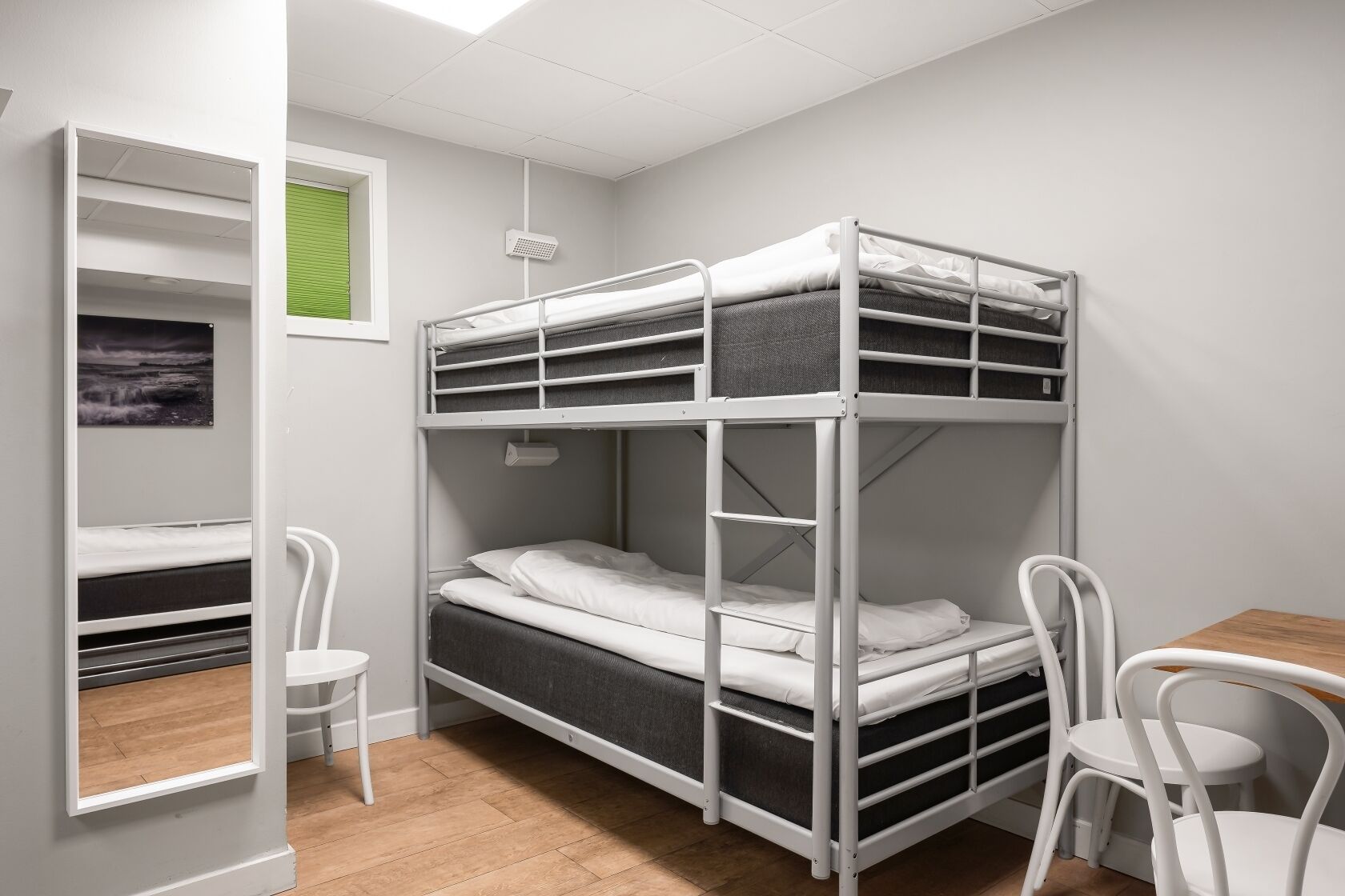 A bunk bed room with a desk and chairs, a window with blinds, and a picture on the wall.