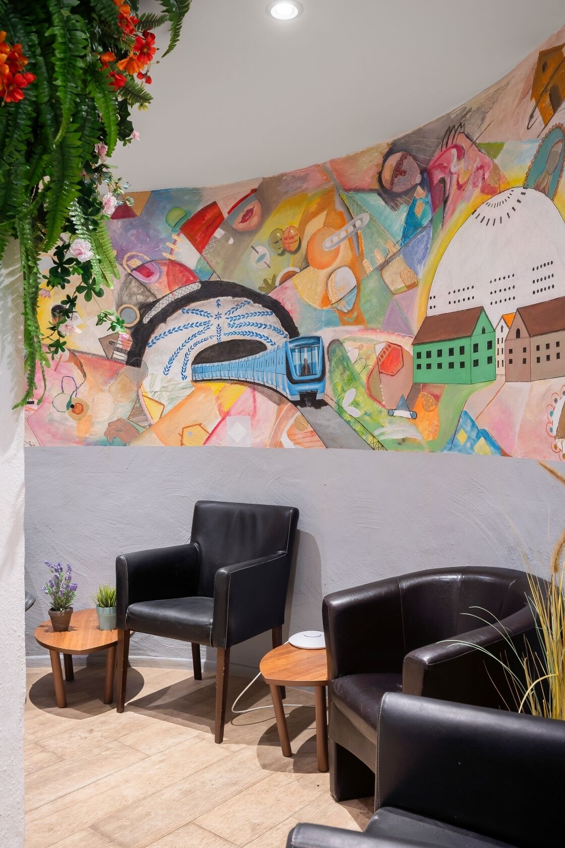 Una habitación con un mural colorido, dos sillones de cuero negro, una pequeña mesa redonda y una planta en maceta.