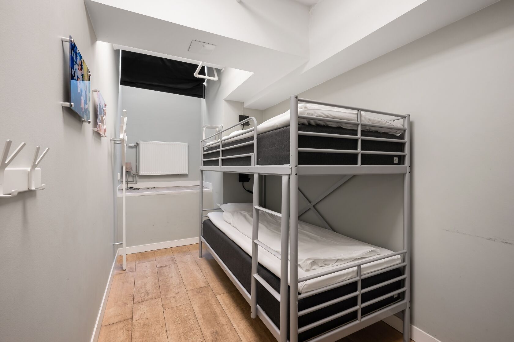 Habitación con literas, un radiador, una ventana pequeña y una puerta que da a otra habitación.
