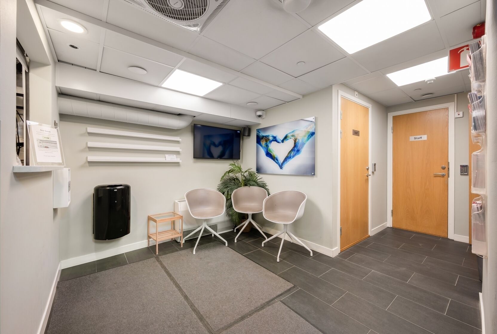 A reception area with a reception desk, two chairs, a plant, and a painting on the wall.
