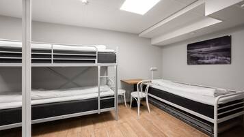 A dormitory room with bunk beds, a desk, a chair, and a painting on the wall.