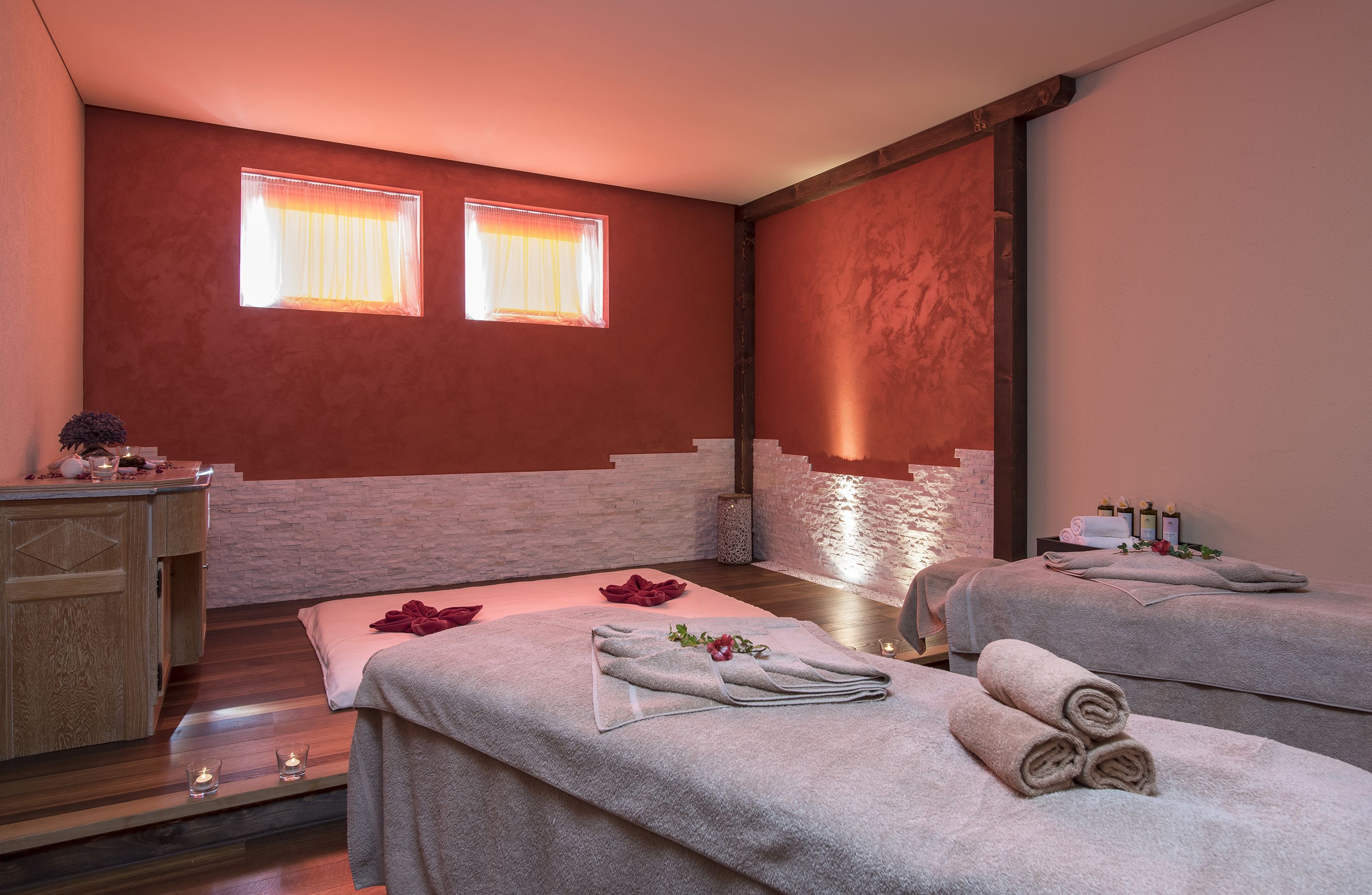 A spa room with two beds, a wooden cabinet, and a small table with candles.