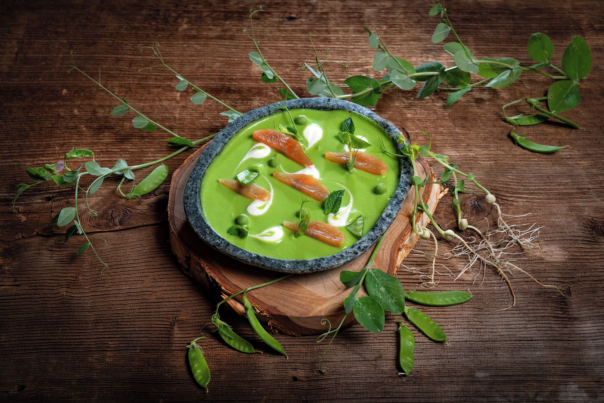 Eine Schüssel grüner Suppe mit Lachs und Sahne auf einer Holzplatte.