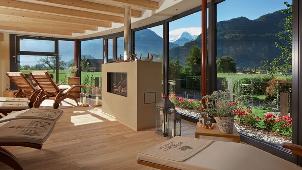 Une chambre moderne dotée de grandes fenêtres, de poutres apparentes en bois au plafond et offrant une vue sur un paysage montagneux.