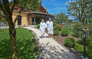 A pathway leading to a modern building with large windows and a covered entrance. - SALZANO Hotel - Spa - Restaurant (Unterseen)