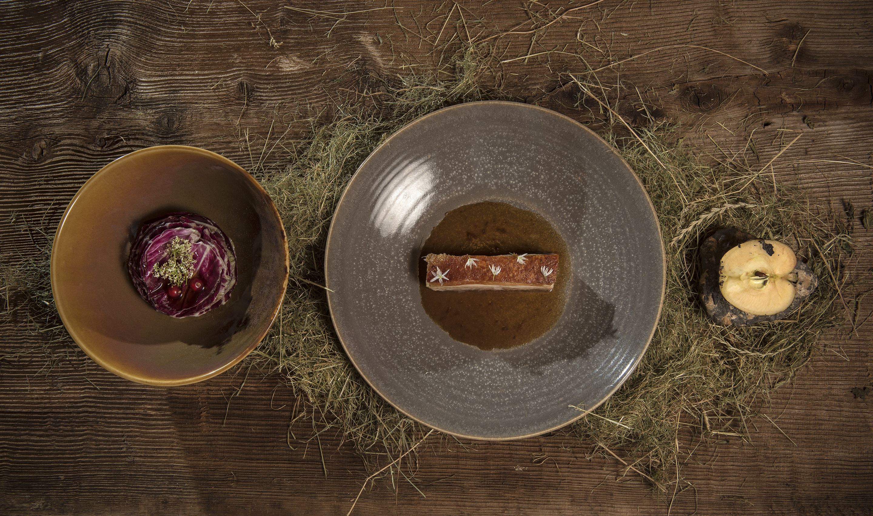 Une table en bois rustique sur laquelle reposent deux plats en céramique : l’un contient une préparation à base de chou rouge, et l’autre, un morceau de viande et un champignon.