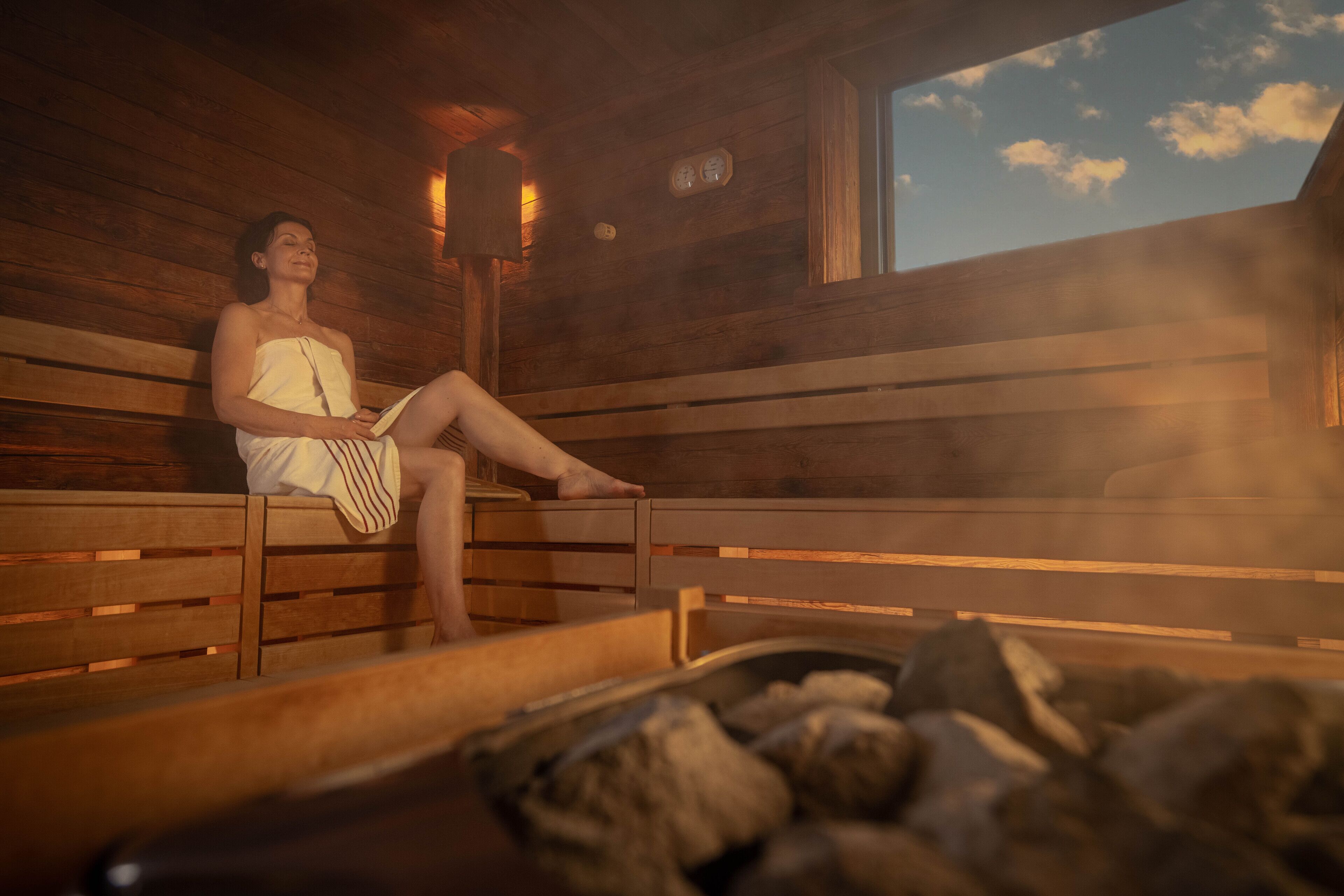 A person sitting on a bench in a wooden cabin with a sauna visible in the foreground.