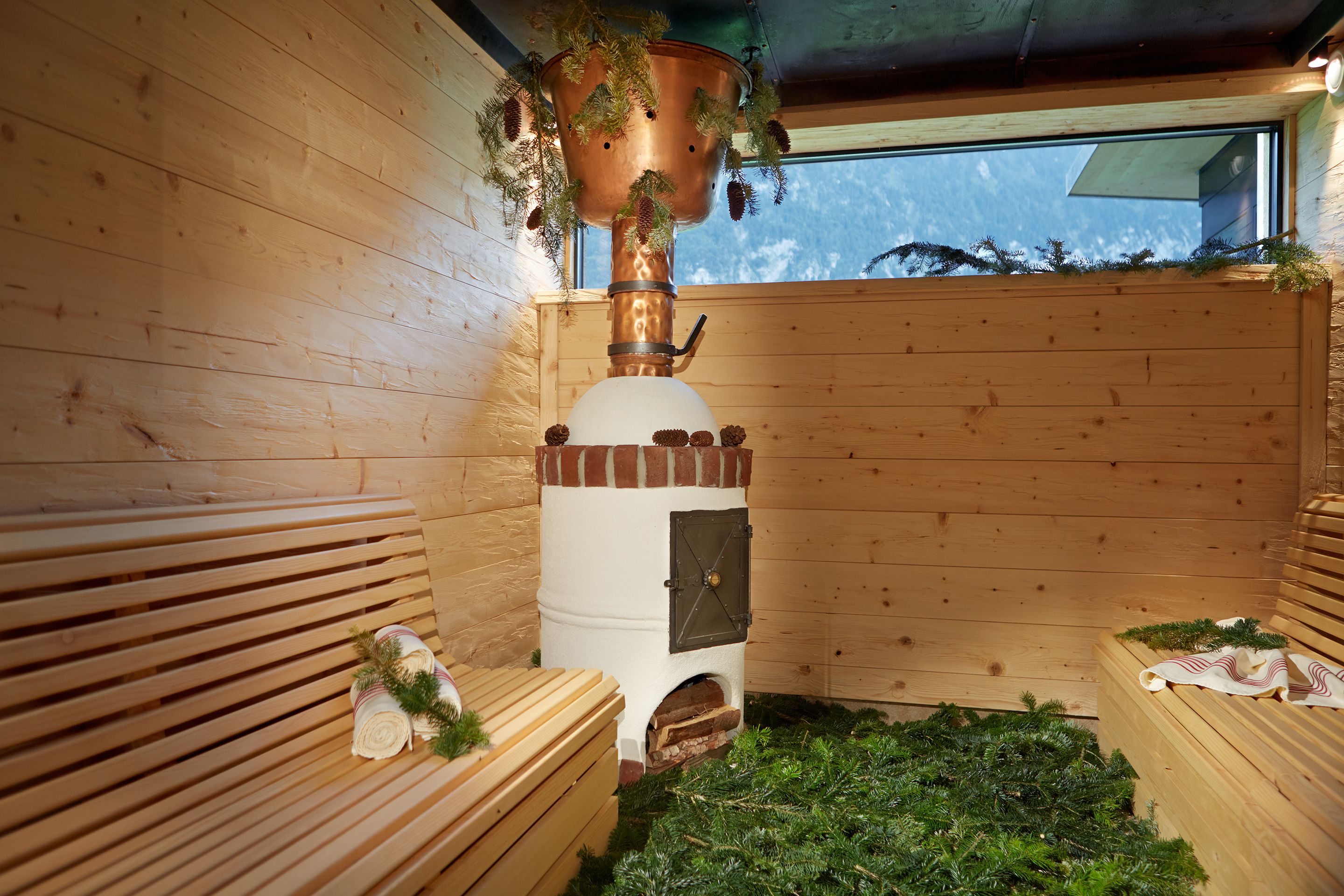 A sauna room with wooden benches, a central steam generator, and a window.