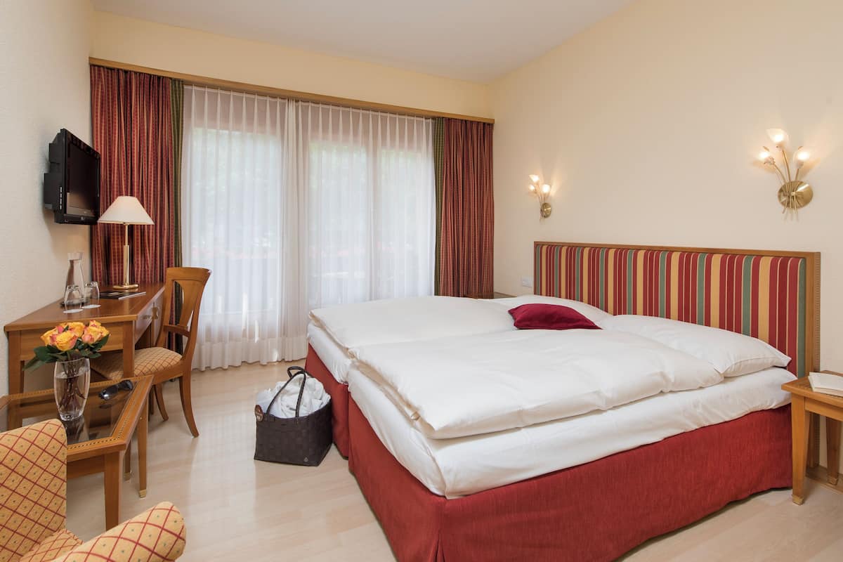 A hotel room with a bed, a desk with a lamp, a chair, a TV, and a window with curtains.