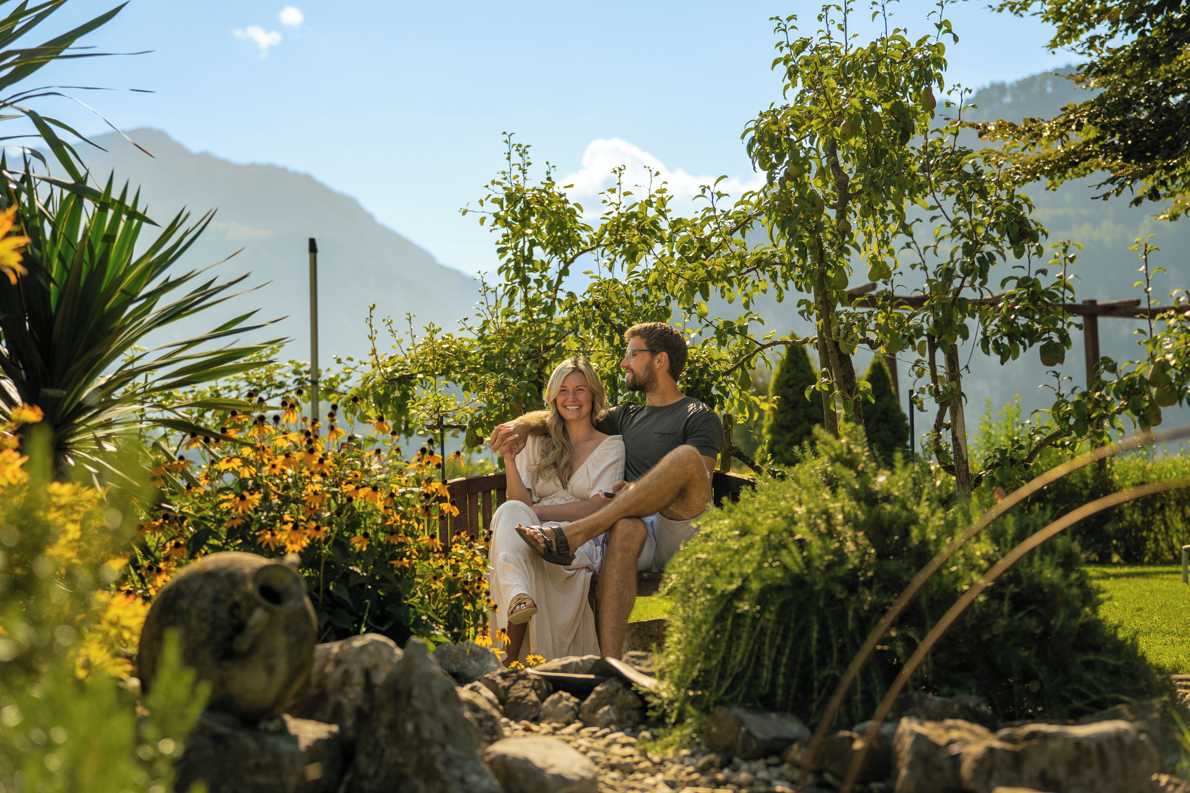 Una pareja sentada en un banco en un jardín, con una montaña al fondo.