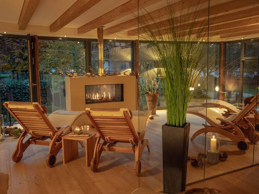 Un interior moderno con chimenea, sillones de madera y grandes ventanas que ofrecen vistas del exterior.