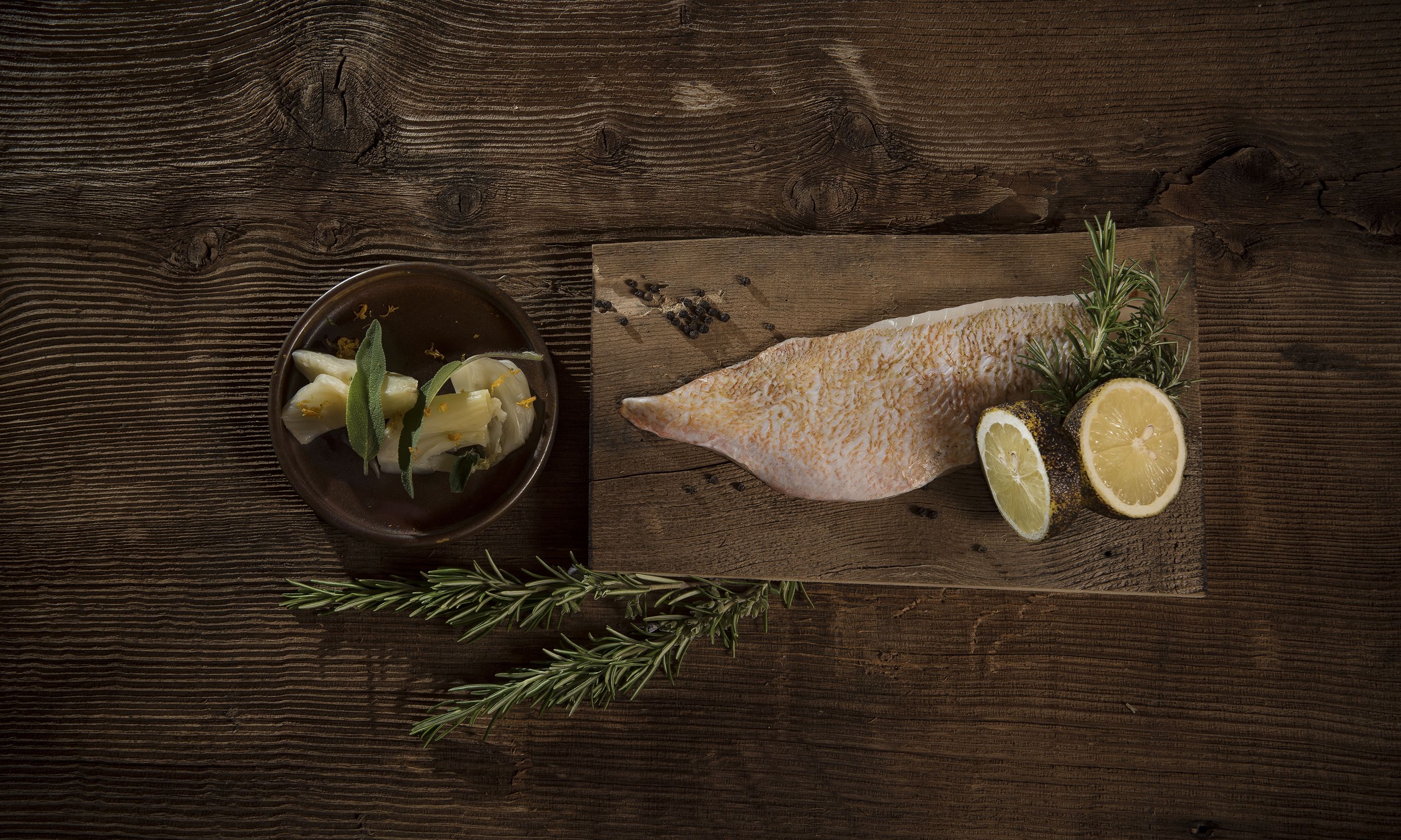 Ein Holztisch mit Fischfilet, Zitronenscheiben und Rosmarin.