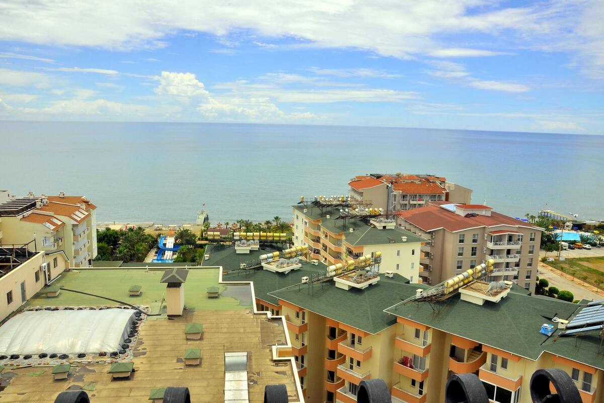 A coastal hotel with multiple balconies, a rooftop pool, and a view of the sea.