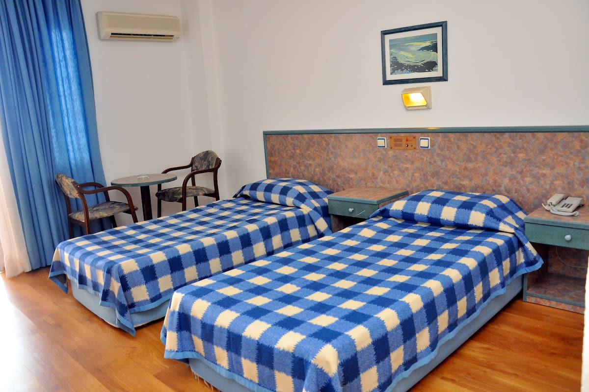 A hotel room with two beds, a small table, a chair, a nightstand with a phone, and a painting on the wall.