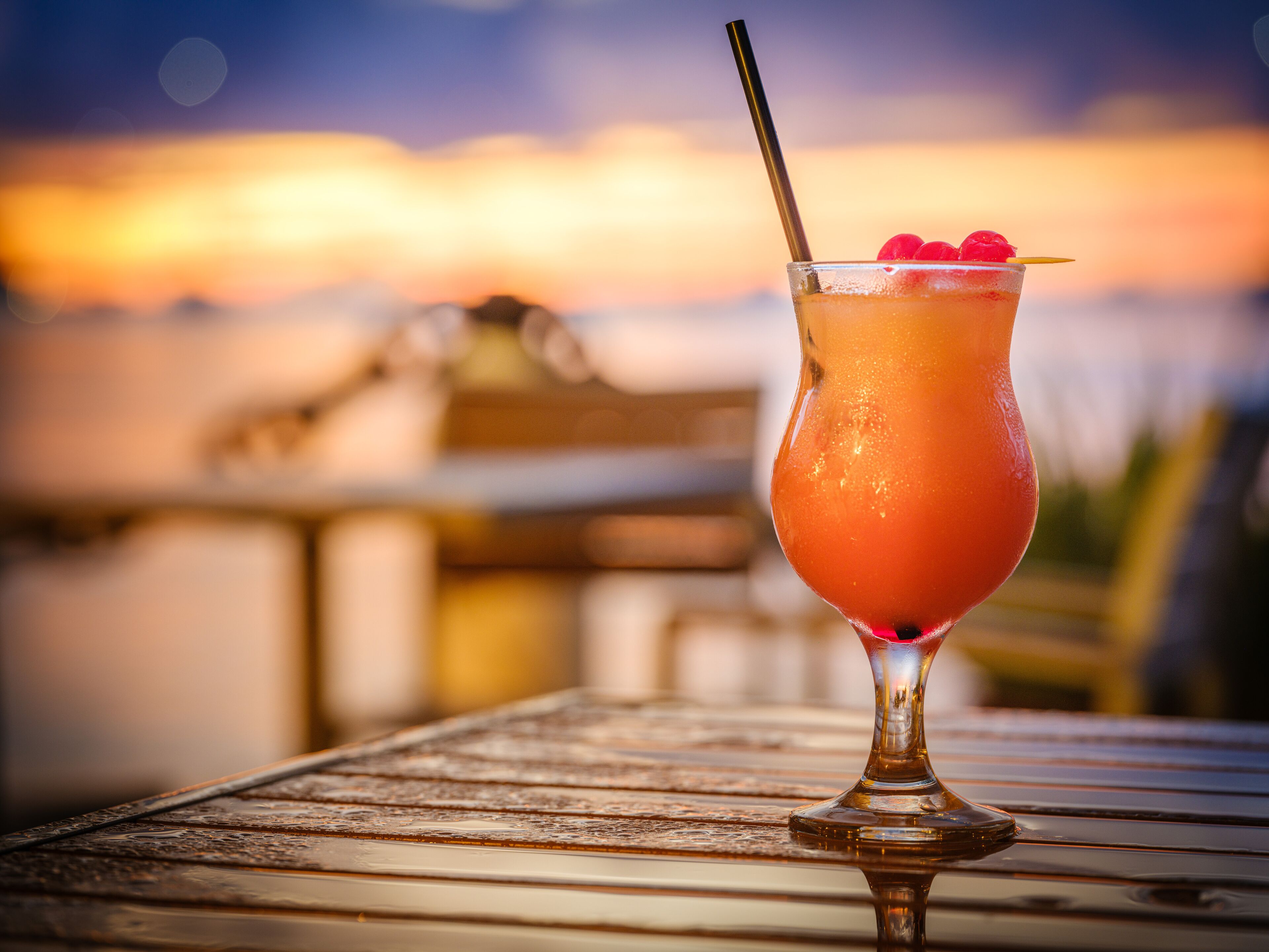 A cocktail on a metal table with a sunset view in the background.