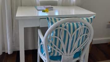 A white table with a striped pillow, a chair with a white frame, and a window with white curtains.