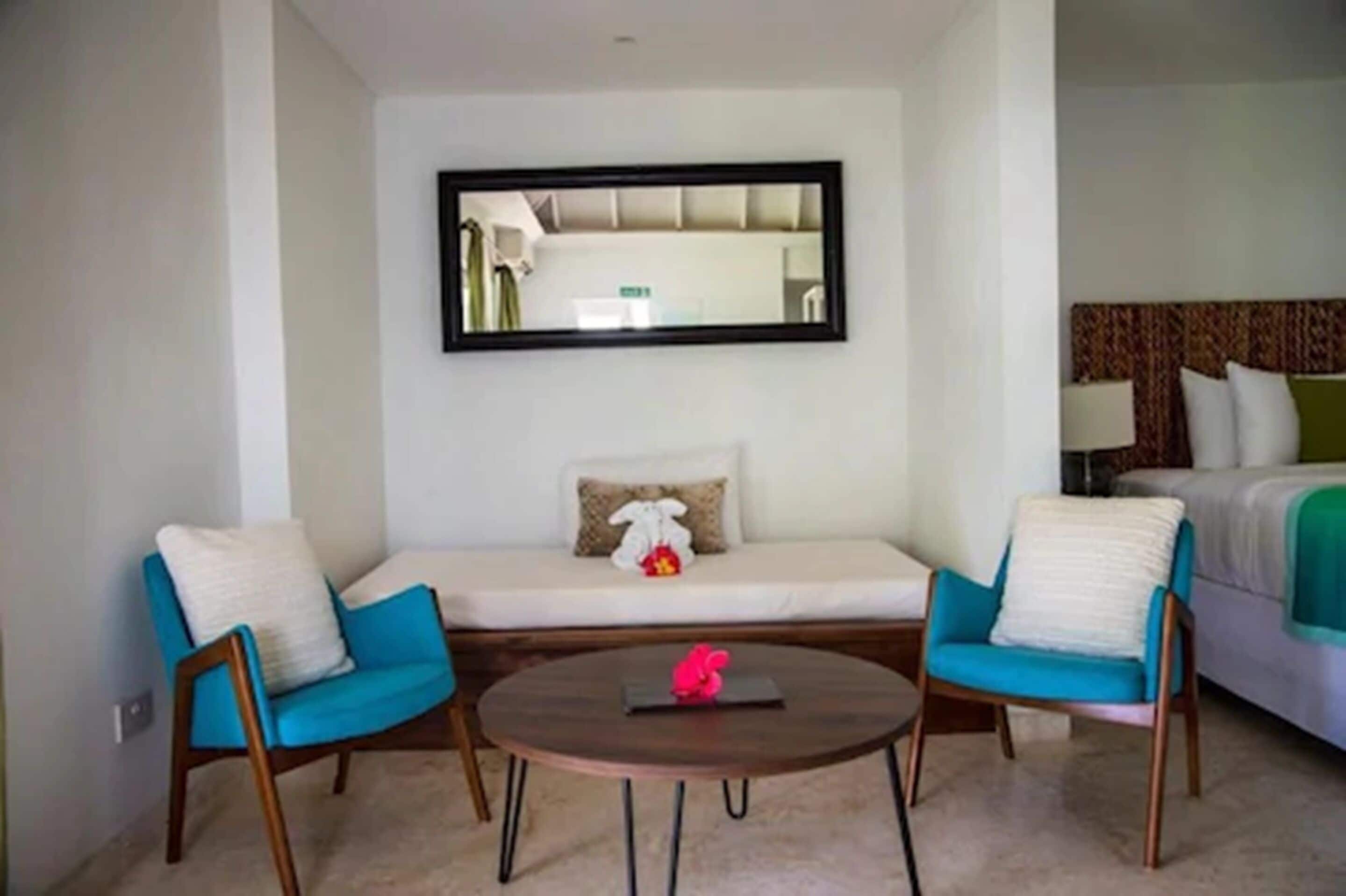 A hotel room with a sofa, two armchairs, a round coffee table, and a bed with a patterned headboard.