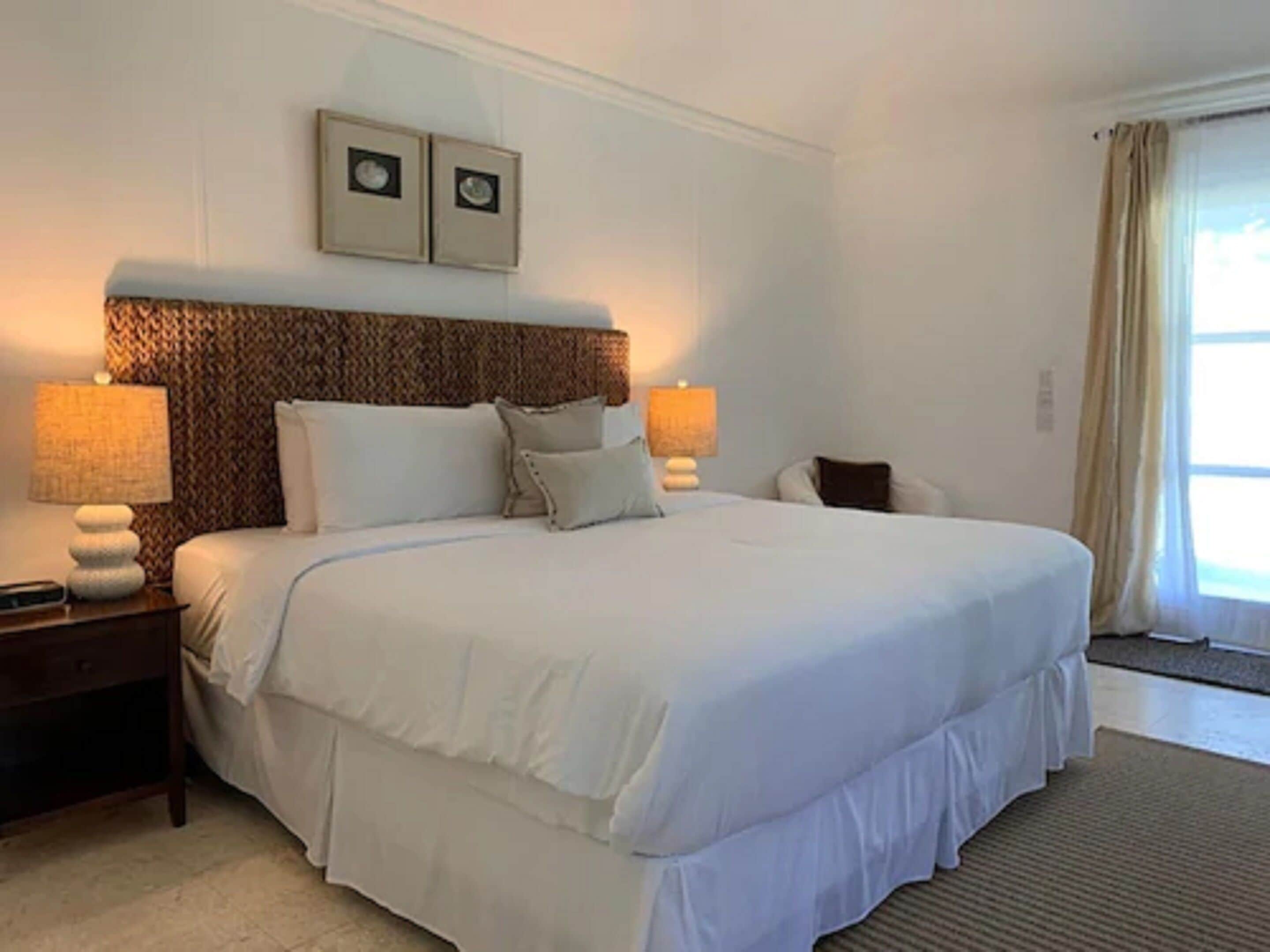 A large bed with white bedding, two bedside lamps, a nightstand, and a headboard with a textured pattern.