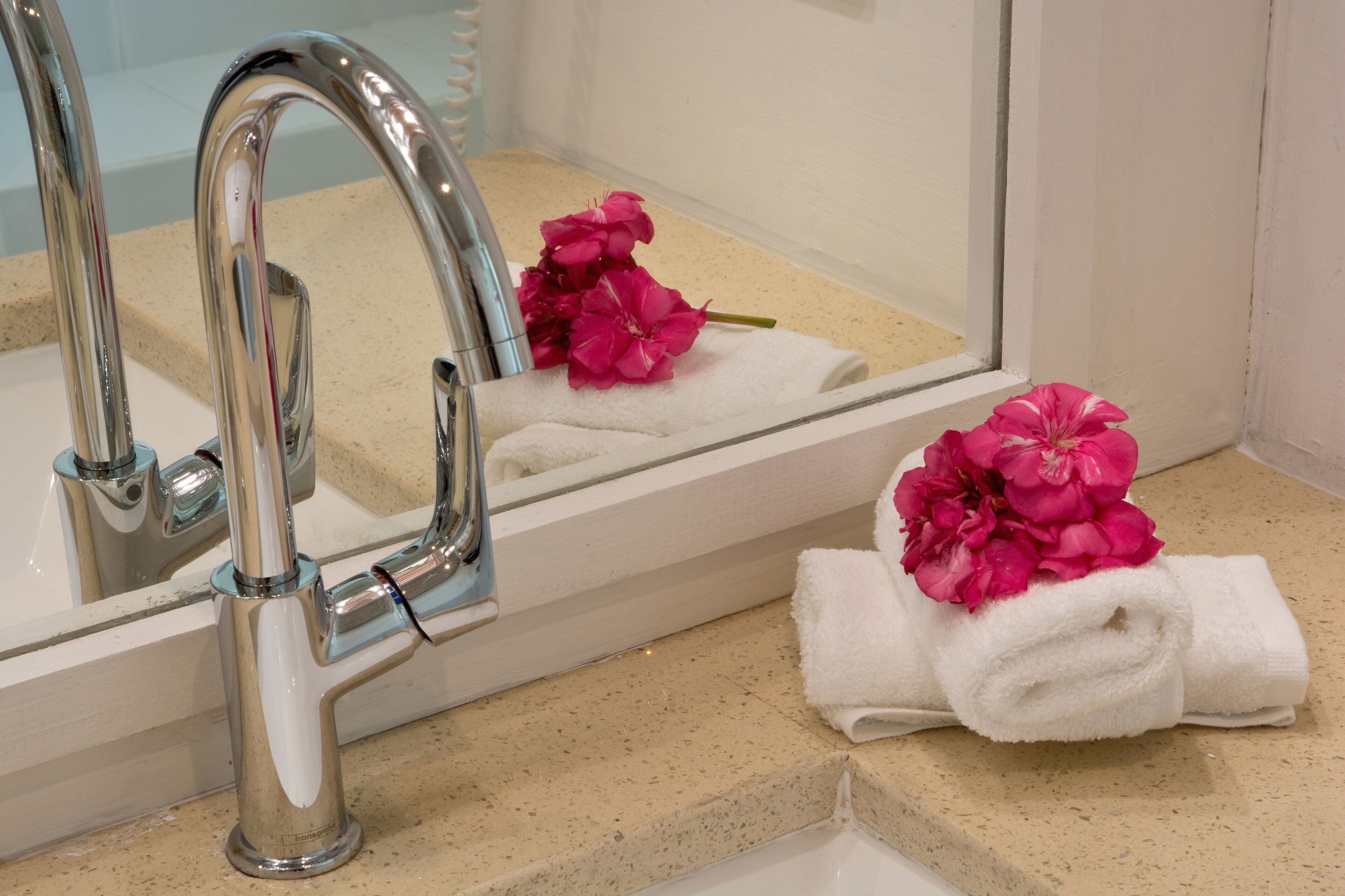 Un baño con grifo de cromo, un espejo y una toalla con motivos florales en rosa.