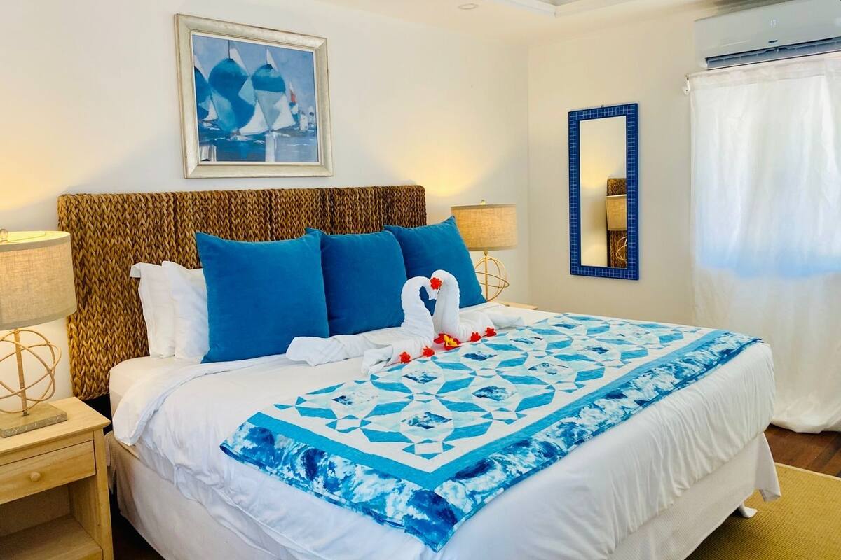 Una habitación de hotel con una cama, un cuadro enmarco, un espejo y una ventana con cortinas.