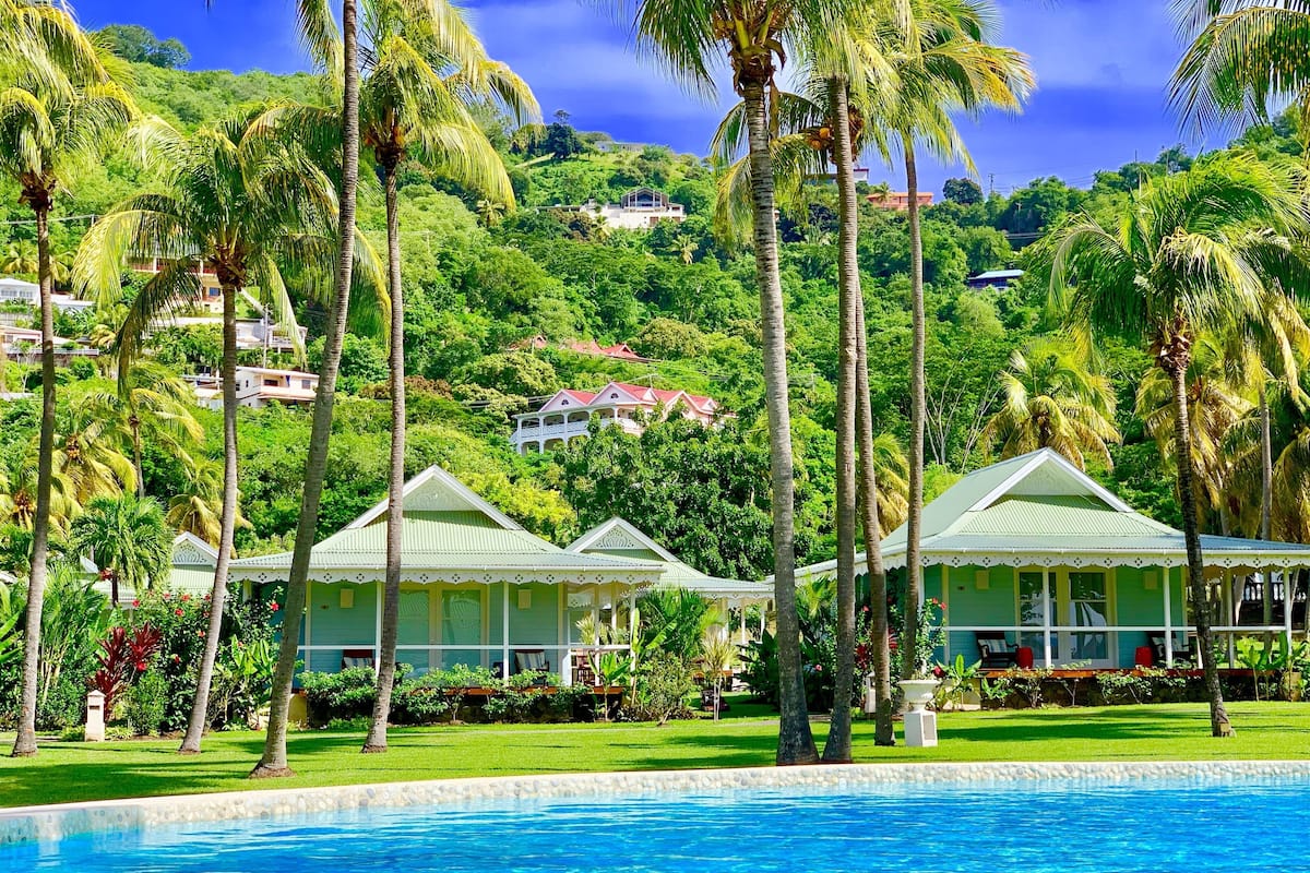 Vista de la piscina en un resort, con varios edificios de techos verdes, rodeado de palmeras y vegetación exuberante.