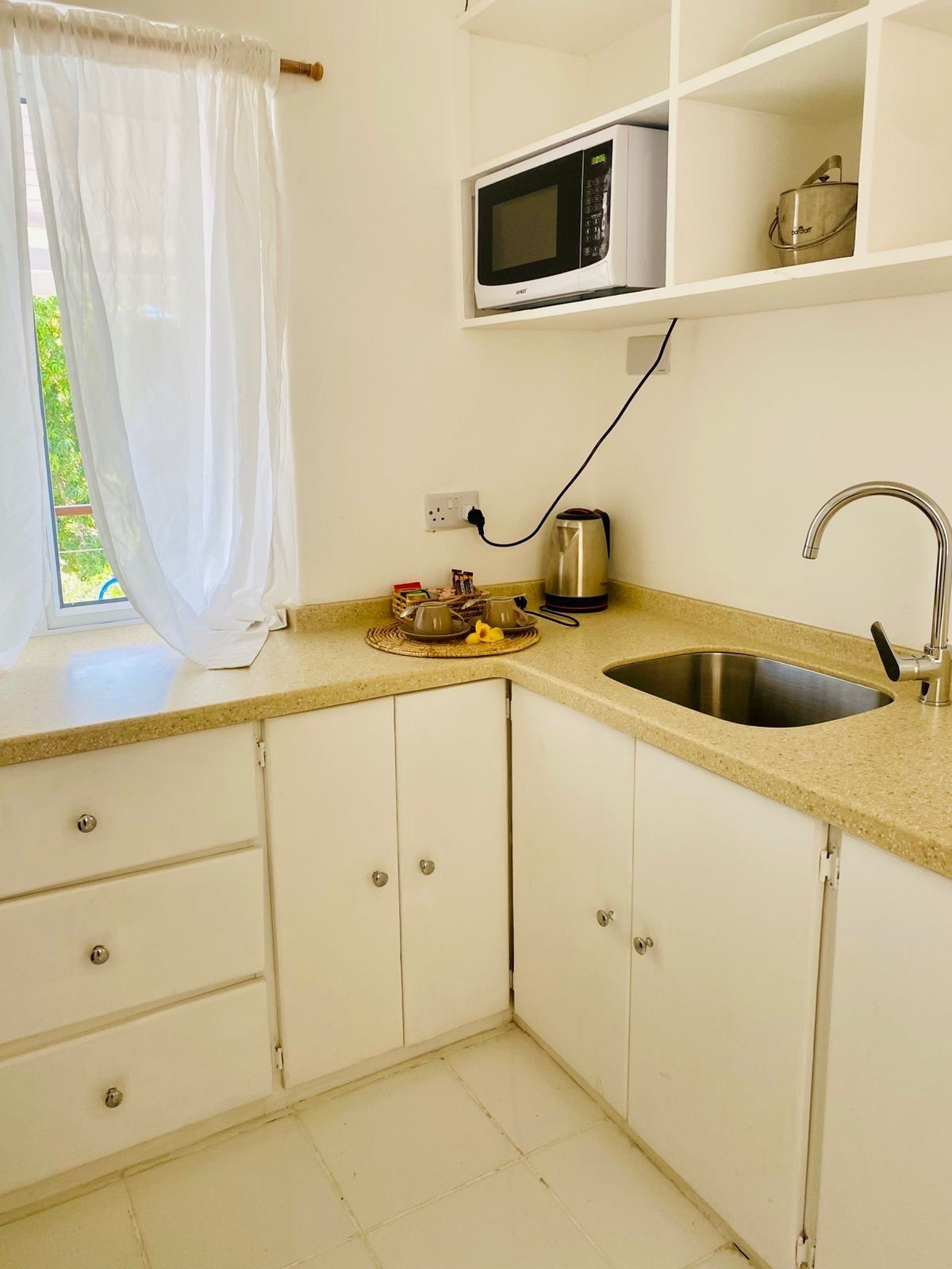 A kitchen with a microwave, kettle, and sink.