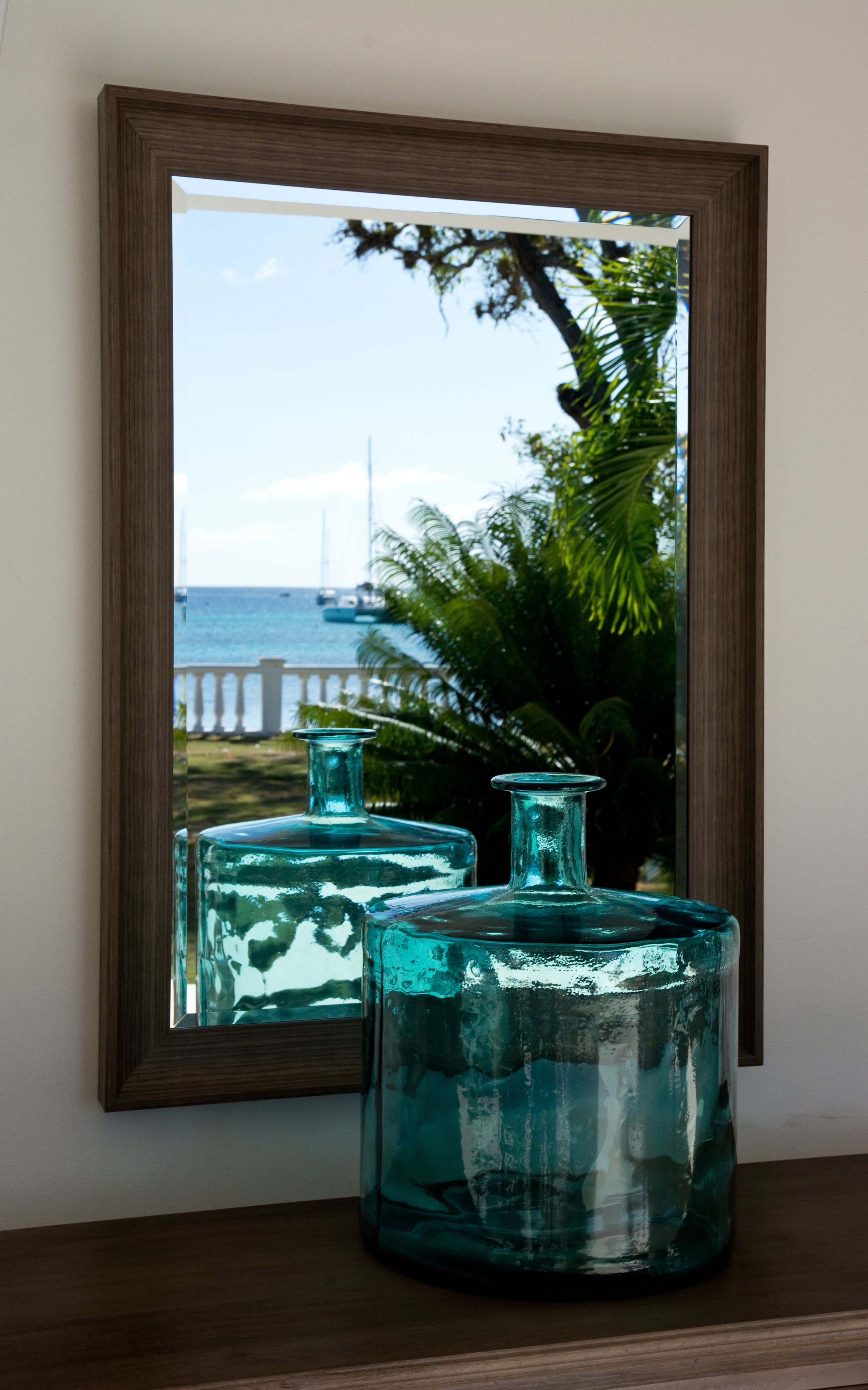 A mirror reflecting a beach scene with two glass bottles on a wooden surface.