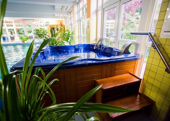 Un jacuzzi con escalones de madera que lo conducen, rodeado de plantas en macetas y vista a una piscina.