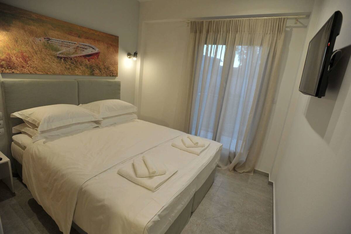 Ein Hotelzimmer mit einem Bett, einem Bild an der Wand, einem an der Wand befestigten Fernseher und einem Fenster mit Vorhängen.