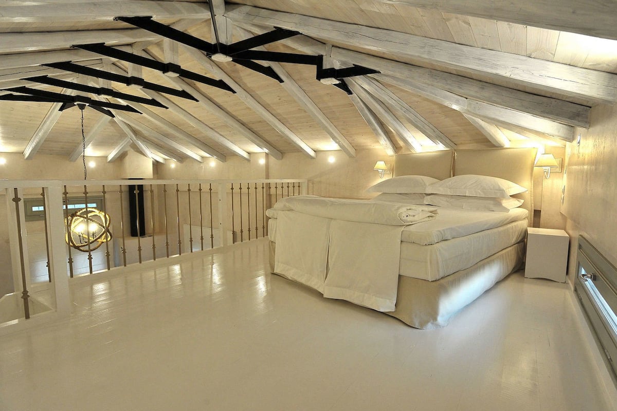 Ein Schlafzimmer mit schrägen Wänden, einem Bett, einem Nachttisch und einer Wandlampe.