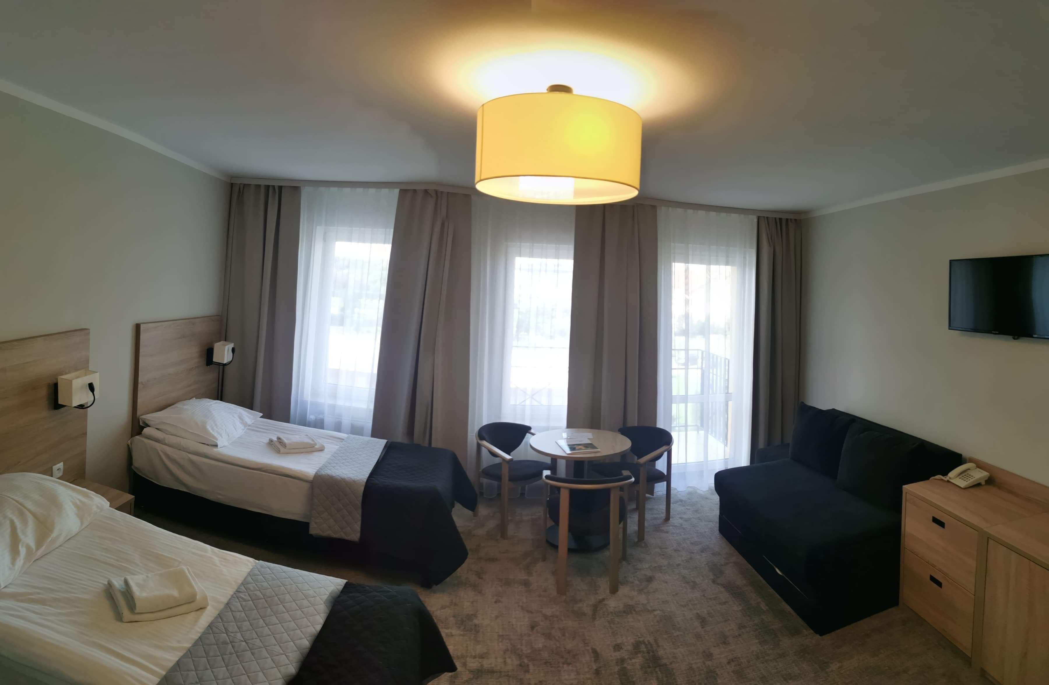 A hotel room with two beds, a sofa, a small table, and a TV.