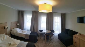 A hotel room with two beds, a sofa, a small table, and a TV.