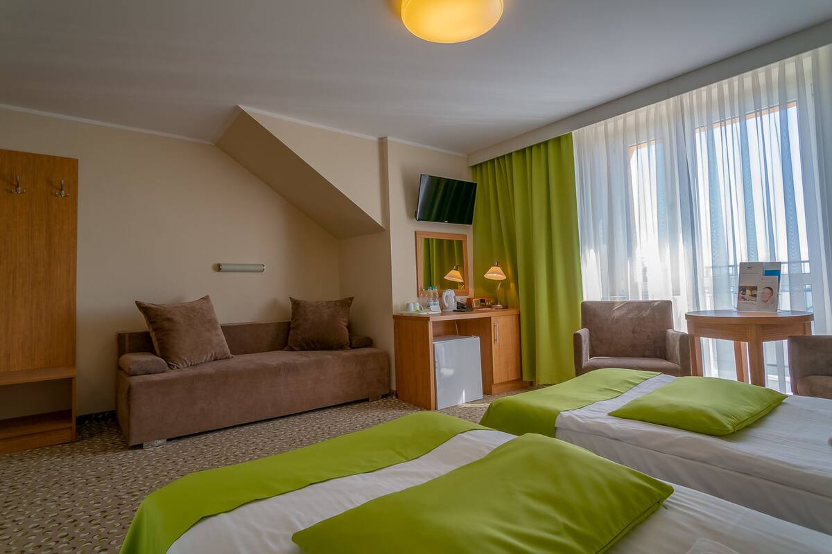 A hotel room with two beds, a desk, a chair, a sofa, and a TV.