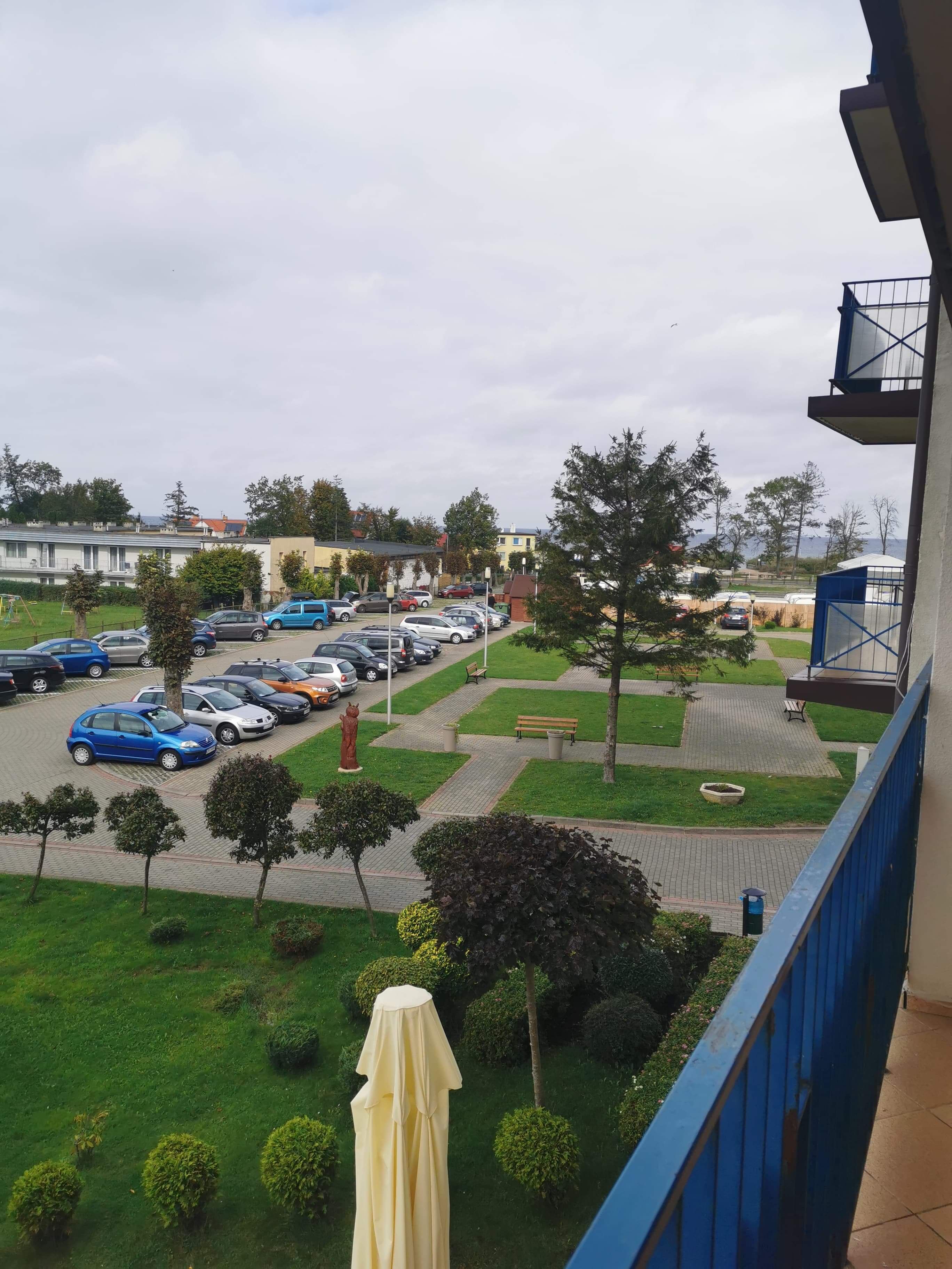 A parking lot with several cars, a statue, and a grassy area with trees and benches.