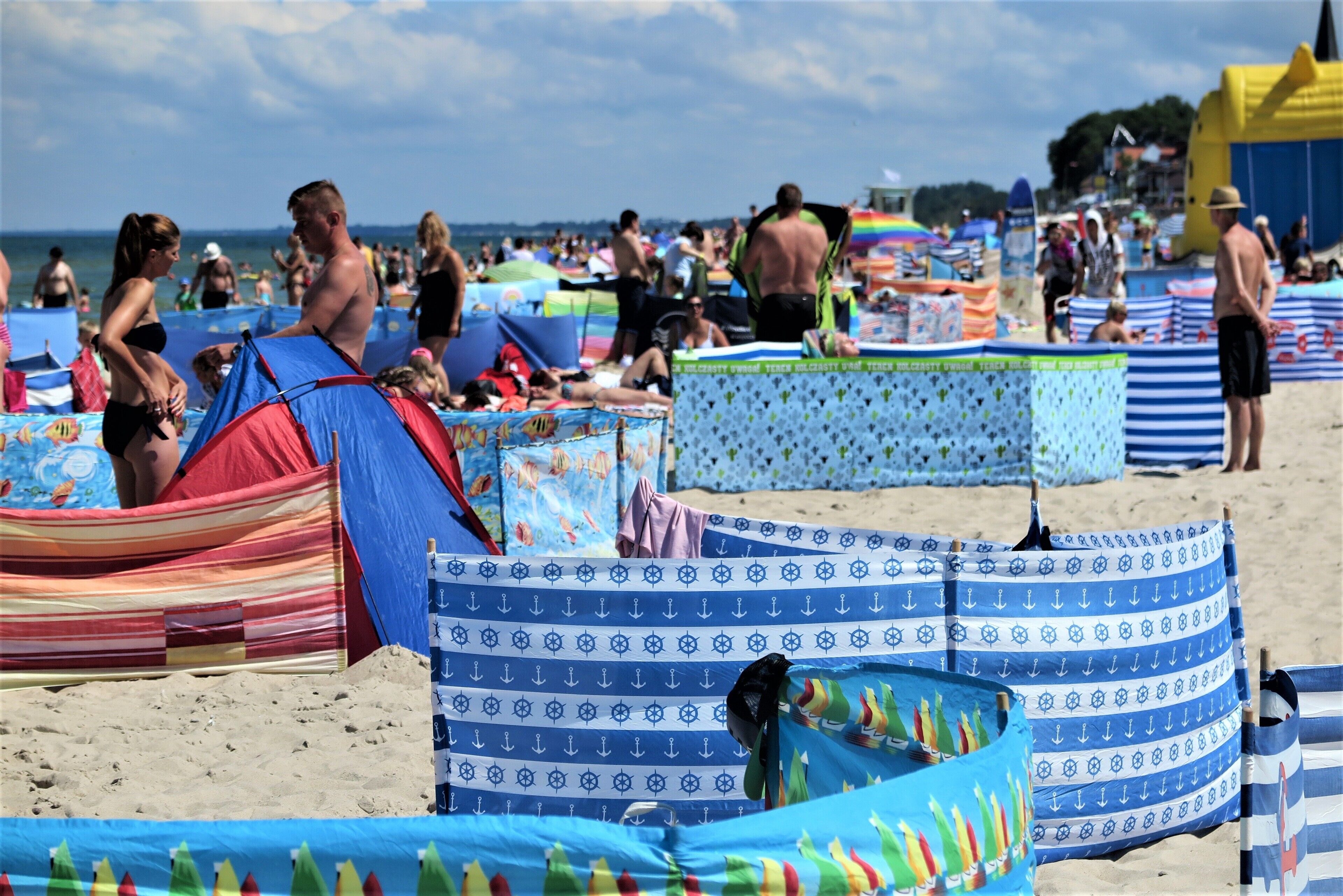 A beach with tents and umbrellas, sandy ground, and people.