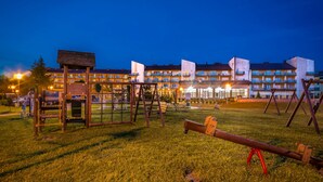 A playground with swings and a seesaw in front of a building with multiple balconies. - Hotel NAT Sarbinowo (Sarbinowo)