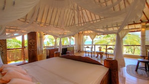 Una habitación amplia con una cama grande, un escritorio de madera y vistas a palmeras y al océano.