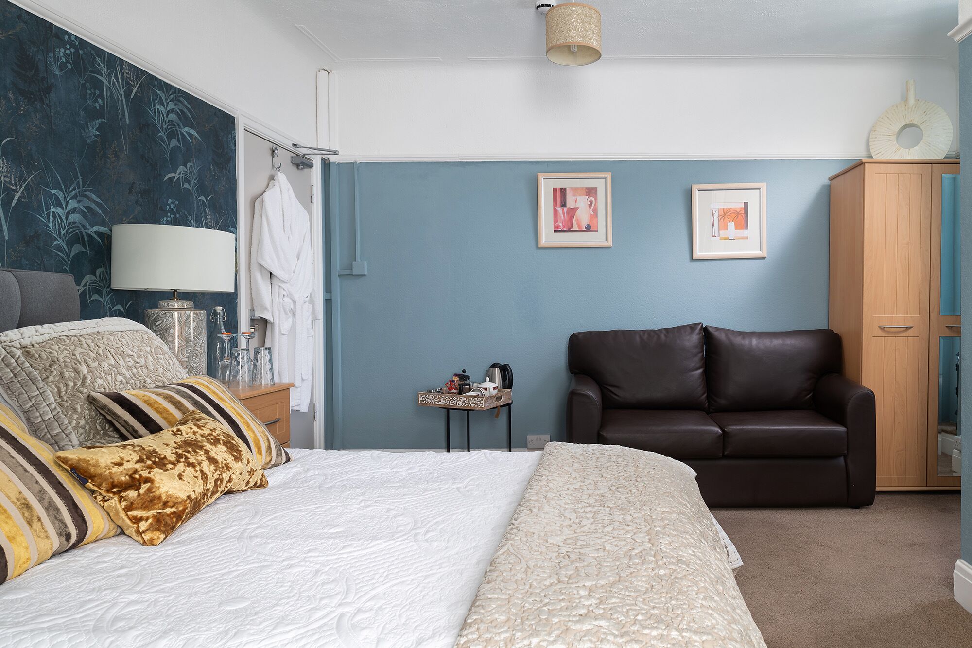 A bedroom with a bed, a leather chair, a wooden wardrobe, and two framed pictures on the wall.