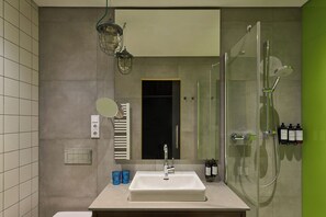 A bathroom with a white sink, a mirror, a glass shower enclosure, and a green accent wall.